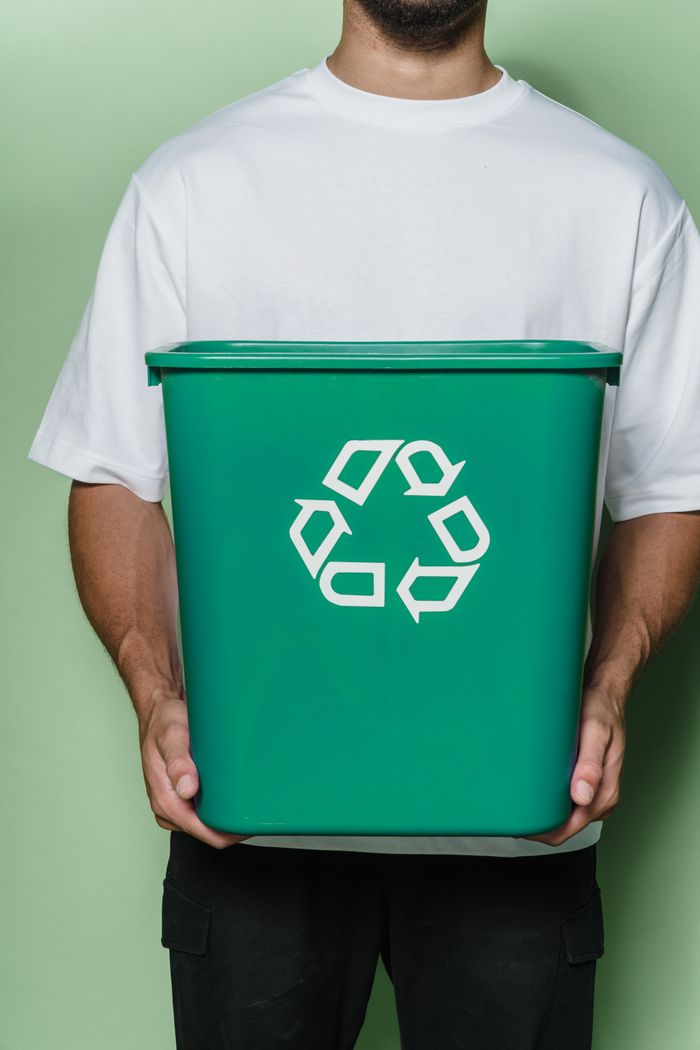 services-03 Adult male holding a green recycling bin against a green background, promoting sustainability.