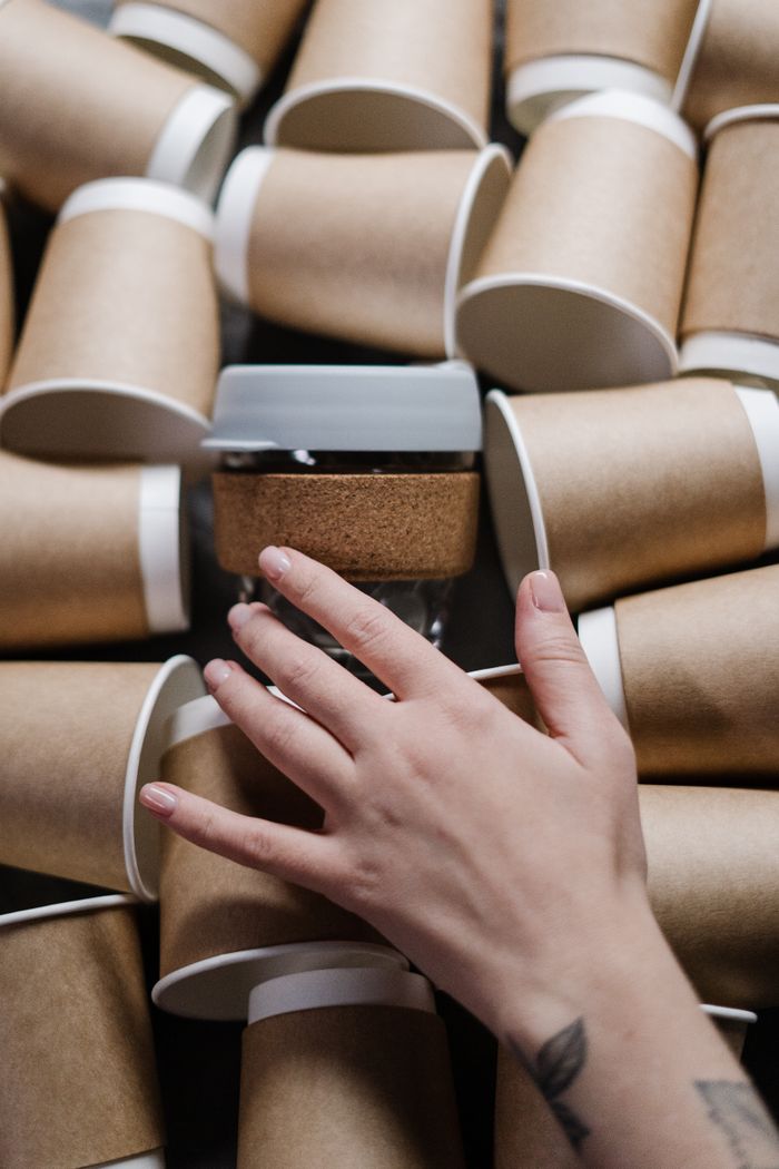 Eco-friendly paper cups with a hand reaching for a reusable coffee cup.